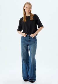 Czarna, oversize koszulka z krótkim rękawem, w zestawieniu z niebieskimi dżinsami o wysokim stanie i rozkloszowanym kroju. Gładka tekstura denimu i szerokie nogawki.
