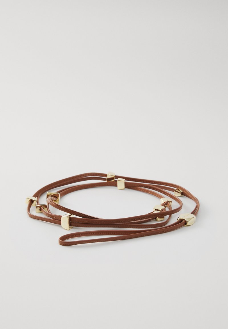 Brown leather strap bracelet featuring gold geometric accents. The design includes multiple intertwined strands with smooth texture.