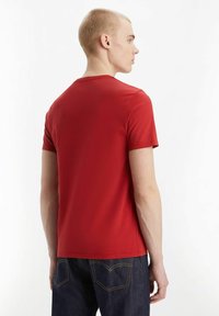Camiseta de algodón roja con cuello redondo y mangas cortas, vista desde la parte de atrás, combinada con jeans de denim azul oscuro.