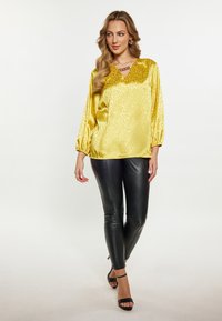 Yellow leopard print satin blouse with a v-neckline, paired with black fitted leather pants and black heeled sandals.