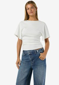Balts ribots īsroku tops ar pieguļošu siluetu un vaļ īgām piedurknēm, kombinēts ar augsta vidukļa zilām džinsa plašajām biksēm.
