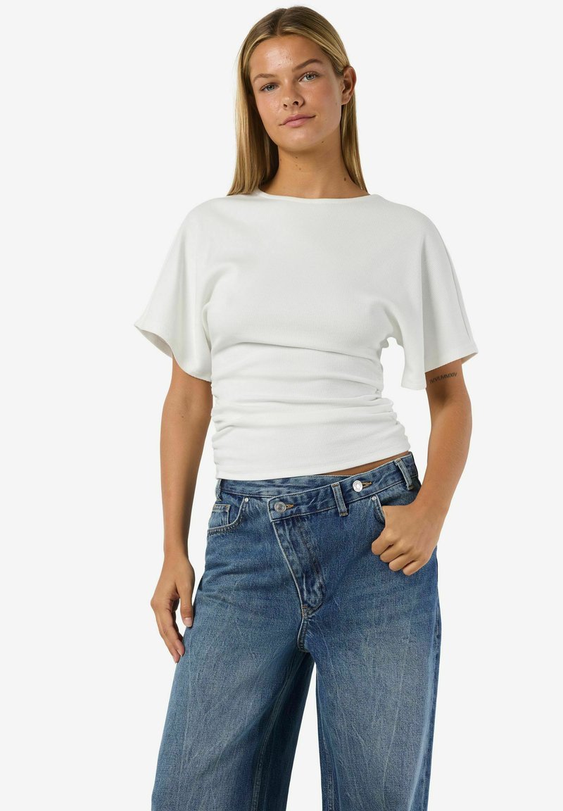 Balts ribots īsroku tops ar pieguļošu siluetu un vaļīgām piedurknēm, kombinēts ar augsta vidukļa zilām džinsa plašajām biksēm.