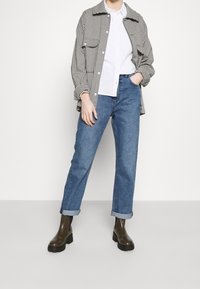 Svart- och vitrutigt overshirt, lager på en vit skjorta med knappar, tillsammans med blå jeans och mörkgröna ankle boots. Avslappnad look, allt i rak passform.