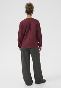 Bordeaux langærmet top med broderi på ærmerne, sammen med grå stribede vide bukser. Blødt stof med en afslappet pasform.