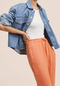 Denim jacket with button closure and two chest pockets, paired with loose, peach-colored pants featuring an elastic waistband.