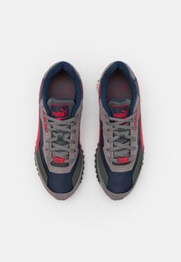 Deux chaussures de sport avec une palette de couleurs bleu marine, gris et rouge. Fabriquées en textile et matériaux synthétiques, elles présentent une semelle texturée et un système de laçage.