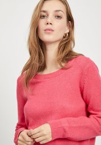 Fuksija pulover s okruglim izrezom, dugim rukavima i rebrastim rubovima, napravljen od mekog, strukturiranog materijala. Istaknut glatkom površinom.