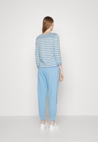 Haut à manches longues rayé bleu clair avec un col rond, associé à un pantalon de style jogger bleu assorti. Le mannequin porte des baskets blanches.