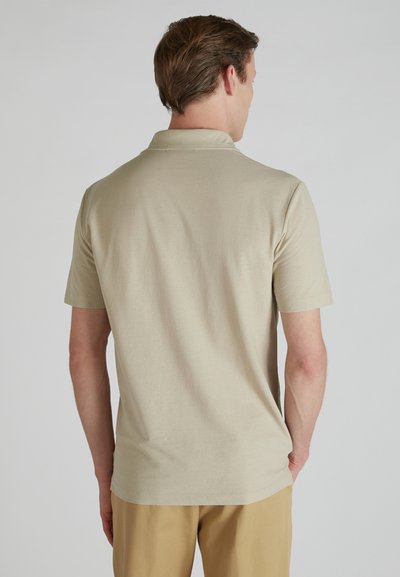 Beżowa krótko rękawowa koszulka polo z gładkiego materiału, z klasycznym kołnierzykiem i luźnym krojem, zestawiona z jasnobrązowymi spodniami.