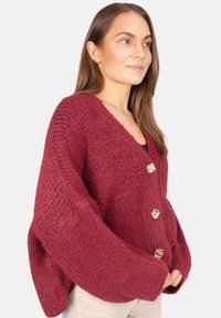 Cardigan en tricot bordeaux avec un décolleté en V profond, de grands boutons et des manches larges, mettant en avant un tissu texturé et une coupe ample.