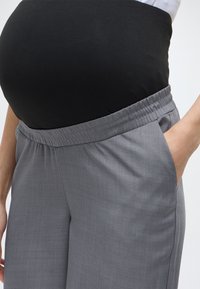 Γκρι παντελόνι εγκυμοσύνης με ελαστική μέση, διαθέτει πλαϊνές τσέπες και απαλής υφής ύφασμα, σχεδιασμένο για να προσαρμόζεται σε μια αυξανόμενη κοιλιά.