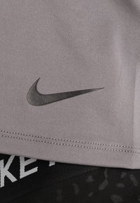 Top atlético gris con el logotipo negro de Nike. Tiene una textura suave y mangas cortas, combinado con una banda elástica negra con diseño debajo.