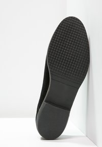 Sole di scarpa in suede nero con un fondo in gomma testurizzato con piccoli motivi a quadrato. Punta leggermente arrotondata e bordo liscio.