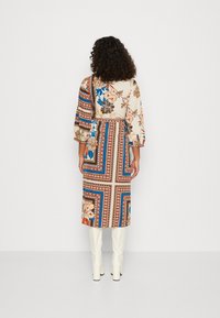 Langarmige jurk met een bloemdessin, met een beige basis en blauwe, rode en bruine accenten, een versmallende taille en een vloeiende rok.