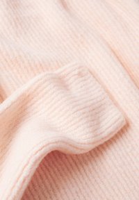 Tissu tricoté doux et rose pâle avec un revers côtelé plié, montrant la texture et les détails fins des points.