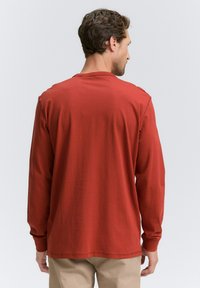 Langärmliges Shirt in rostfarben, aus weichem Stoff. Mit Rundhalsausschnitt und gerippten Bündchen; einfaches und nahtloses Rückendesign.