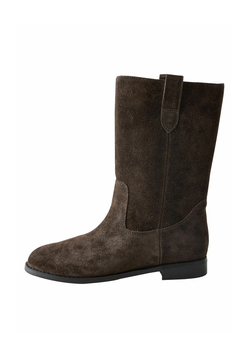 Botte en daim marron hauteur genou avec une texture lisse, un bout rond et une petite languette sur la tige. Semelle plate avec un minimum de détails.
