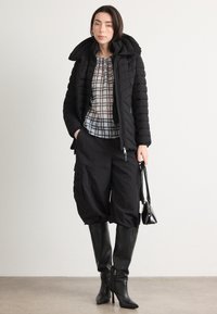 Giacca a vento nera con colletto alto, indossata sopra una camicia a scacchi. Pantaloni cargo neri larghi e stivali neri con tacco al ginocchio. Borsa nera.