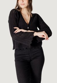 Pull en tricot noir cropped avec un décolleté en V, un ourlet à volants et des manches évasées présentant un motif en maille ouverte.