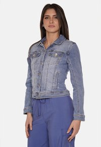 Giacca di jeans azzurro chiaro con taglio classico, due tasche frontali, bottoni decorativi e una texture leggermente scolorita. Design aderente.