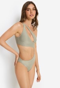 Πράσινο μεταλλικό μπικίνι με σχέδιο με ανοίγματα, που διαθέτει τοπ με βαθύ V-λαιμόκοψη, φαρδιές τιράντες και αντίστοιχο ψηλόμεσο κάτω μέρος με λεία υφή.