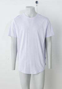 Šviesiai violetinė medvilninė marškinėliai su trumpomis rankovėmis, apvalia apykakle ir šiek tiek išlenktu apačios kraštu. Lygus tekstūra, minimalus dizainas.