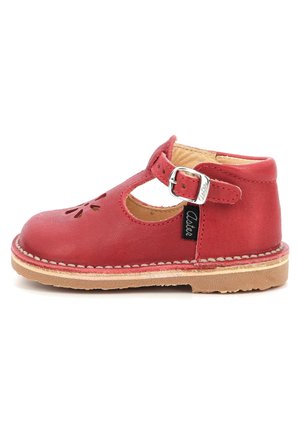 Zapato de cuero rojo con diseño de tira en T, patrones de flores recortados en la punta, una hebilla plateada y una suela de goma color marrón claro.