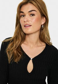 Haut en tricot noir à côtes avec un décolleté en keyhole orné d'une perle. Manches longues et design texturé sur l'ensemble.