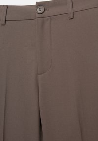Krupni plan hlača boje taupe s detaljima dugmadi, pojasom s petljama i prednjim džepom.