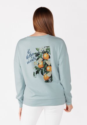 Felpa azzurra chiara con maniche lunghe, che presenta una grafica di arance e fiori sulla schiena, con il testo "il dolce" in un font scuro.