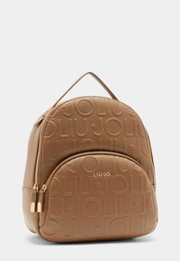 Zaino in pelle tan con motivo a logo in rilievo, forma arrotondata, tasca frontale con zip e manico superiore per il trasporto. Dettagli in metallo dorato.
