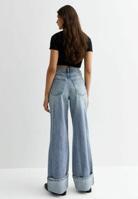 Jeans de mezclilla azul claro de cintura alta con piernas anchas, dobladillos deshilachados y dos bolsillos traseros, combinados con un top negro corto.