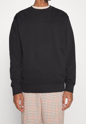 Schwarzer Baumwollpullover mit Rundhalsausschnitt, langen Ärmeln, gerippten Bündchen und einem dezenten Logo auf der Brust, kombiniert mit gemusterten Hosen.