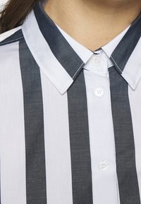 Knapplång skjorta med växlande mörkgrå och vita vertikala ränder, med klassisk krage och slät tygstruktur.