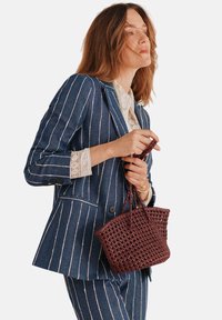 Jeansblazer med vita vertikala ränder, kombinerat med en spetsblus. Håller en liten, vävd bordeauxfärgad handväska.