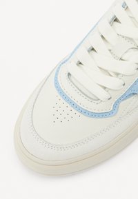 Sneaker con una toma in pelle bianca e accenti in suede blu chiaro, dettagli perforati, completata da lacci bianchi e una suola in gomma color sabbia.