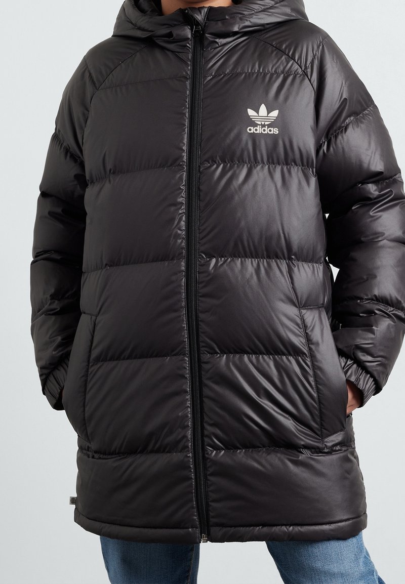 Sort polstret jakke med hætte, der har en lynlåslukning og et hvidt Adidas-logo på brystet. Glat, skinnende overflade med stitched paneler.