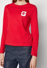 Rood katoen T-shirt met lange mouwen, voorzien van een witte geborduurde "G"-logo op de linkerborst. Gladde textuur, ronde halslijn en aansluitend ontwerp.