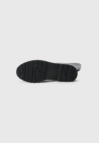 Semelle en caoutchouc noir avec un motif texturé en zigzag. Le design est plat et large, adapté pour offrir adhérence et stabilité.