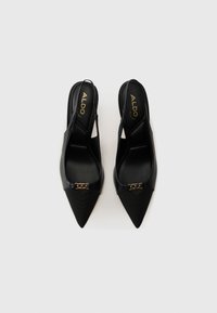 Talons aiguilles noires à bride arrière avec un design à bout pointu, présentant un avant texturé, des accents en cuir lisse et un détail en chaîne dorée sur le dessus.