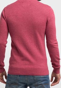 Pull ajusté à manches longues en maille rose chinée. Présente des poignets et un ourlet côtelés. Porté avec un jean bleu, montrant une texture lisse.