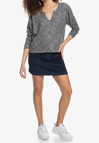 Suéter de punto gris con escote en V, mangas largas y patrón texturizado, combinado con una falda corta de pana azul marino y zapatillas blancas.