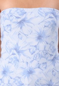 Top senza spalline di colore azzurro chiaro con motivo floreale in tonalità di blu più scure, con dettagli di fiori di ibisco e foglie su un tessuto morbido e strutturato.