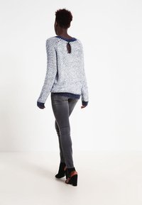 Stickad tröja i blått och vitt, med ett texturerat mönster, långa ärmar och nyckelhål i ryggen. Matchad med grå figurnära jeans och svarta klackar.