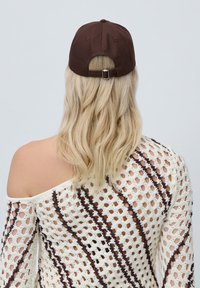 Brown baseball cap with adjustable strap at the back, viewed from the back. Noticeable seam detailing on the curved brim.