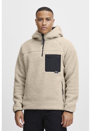 Beige fleece hoodie with a zippered black chest pocket and drawstring hood. Textured fabric, stitched detailing on sleeves and body.