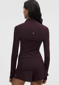 Sügabe, sügav burgundia värvi, pikka varrukat sobiv topp, mis on valmistatud siledast kangast, keskse õmbluse detaili ja väikese logoga taga.