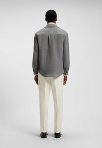 Gray wool blend shirt jacket with a pointed collar, long sleeves, and a rounded hem, paired with white tailored trousers and black shoes.