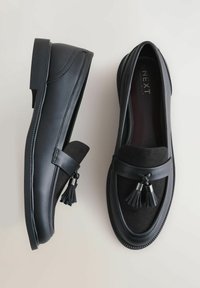 Sorte loafers i glat læder og ruskind, med tassel-detalje på siden, syningsdetaljer og en rund tådesign.