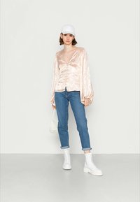 Top de satén rosa com mangas longas, decote em V e detalhe com botões, combinado com jeans azuis arrebitados e botas brancas de tornozelo. Pequeno saco branco incluído.